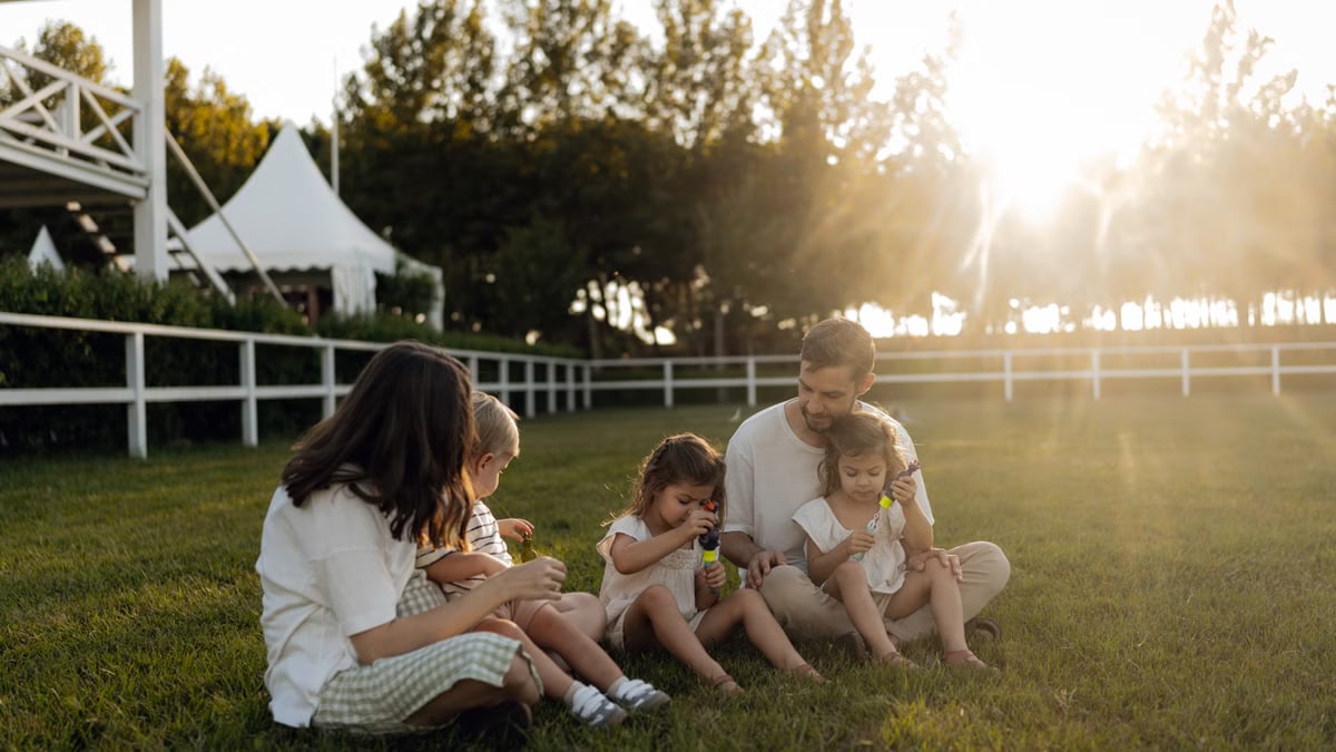 Family sitting on grass enjoying leisure time outdoors, with sun setting in the background.